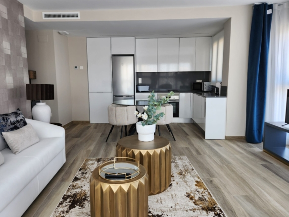 Salón con cocina integrada en tonos blancos y negros, mesa auxiliar dorada, sofá claro y ventanales con cortinas azul marino