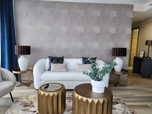 Salón elegante con sofá blanco, mesas auxiliares doradas, lámparas decorativas y pared con papel texturizado en tonos neutros