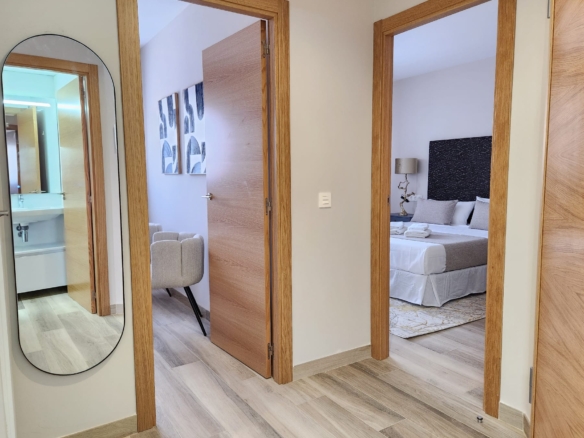 Distribuidor interior con puertas de madera, suelo de madera clara y vistas hacia un dormitorio y un baño moderno