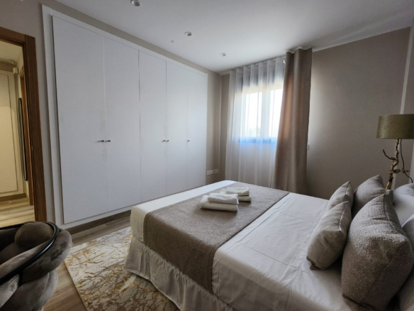 Dormitorio principal con cama doble, armarios empotrados blancos, cortinas claras y decoración en tonos neutros
